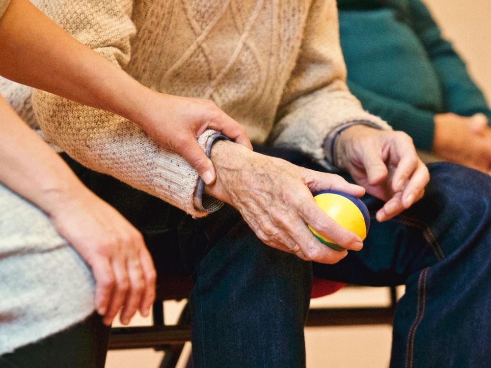 A caregiver's hand resting gently on an older person's arm as they sit together